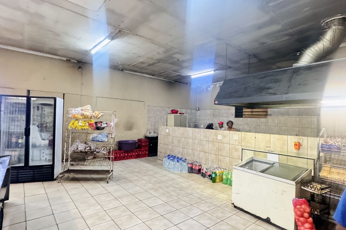 Commercial kitchen area featuring tiled flooring, a large extractor hood, and tiled service counter, requiring significant maintenance and cosmetic updates.