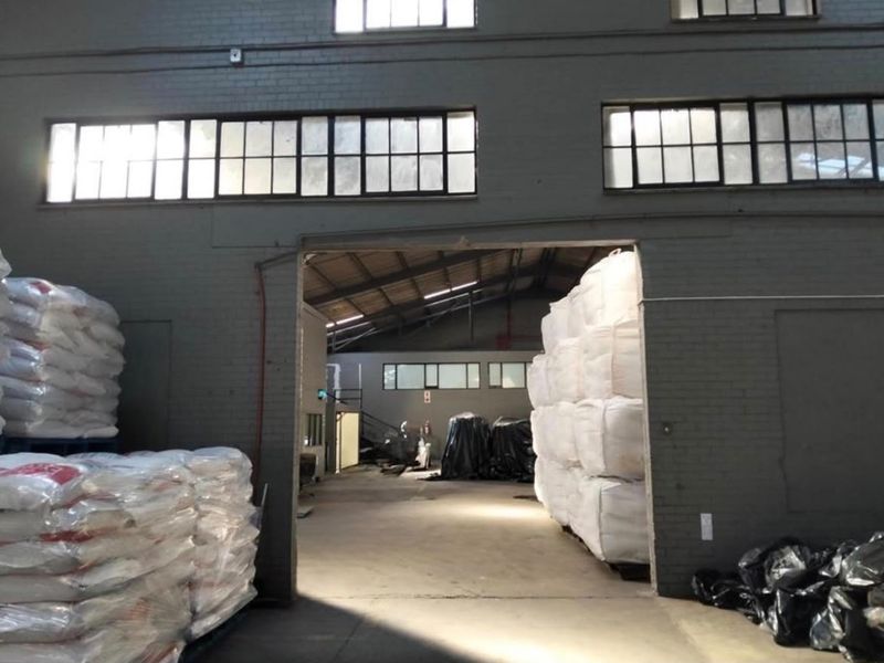 Spacious industrial warehouse interior featuring high ceilings, exposed brick walls, and large steel-framed windows providing natural light to the storage area.