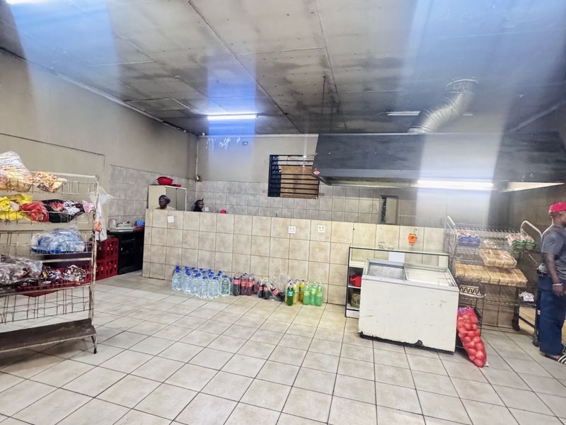 Commercial kitchen area featuring tiled flooring, wall-mounted prep counters, and an industrial extractor hood, suitable for food service operations.