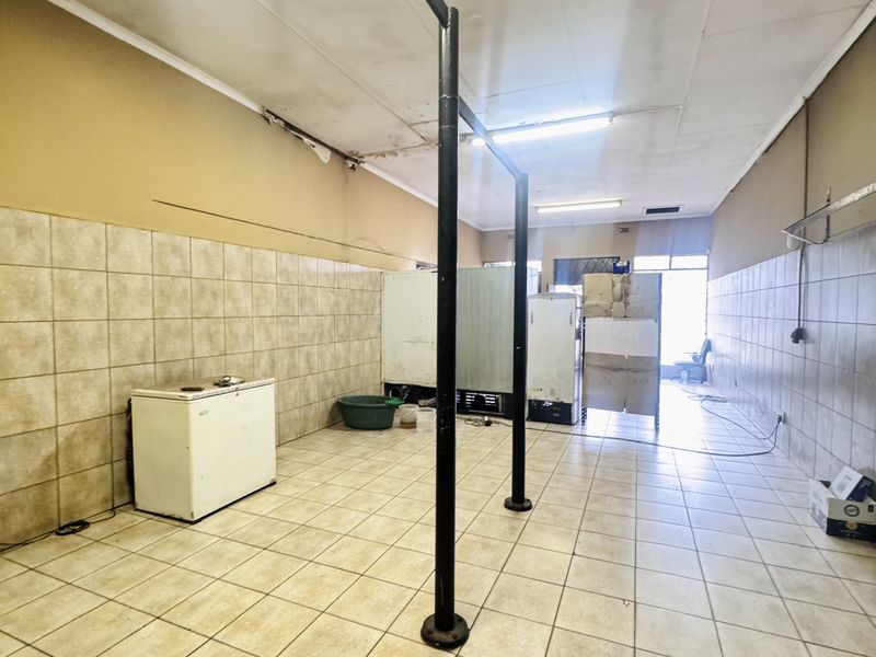 A vacant commercial space featuring tiled flooring, wall tiling, and exposed structural support poles, suitable for retail or service-based business operations.