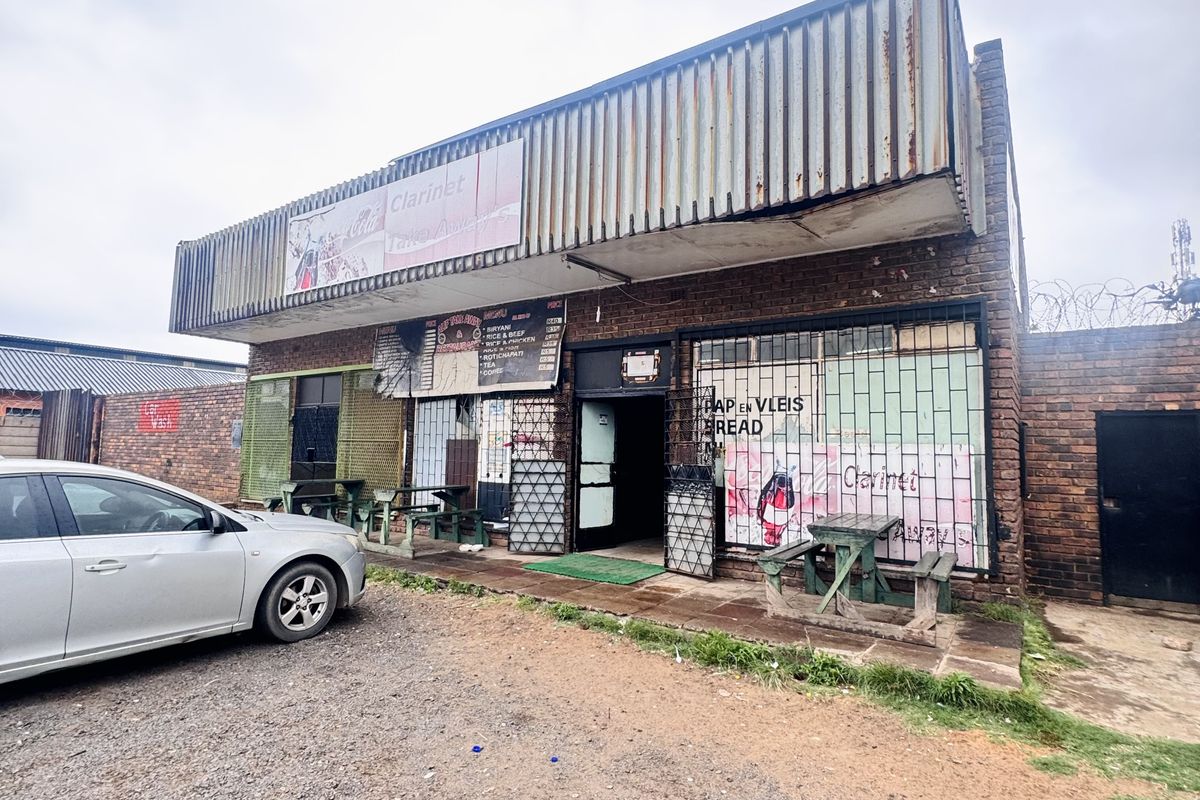 Commercial storefront featuring brick facade, metal signage, security gates, and gravel parking area, suitable for retail or food service business.