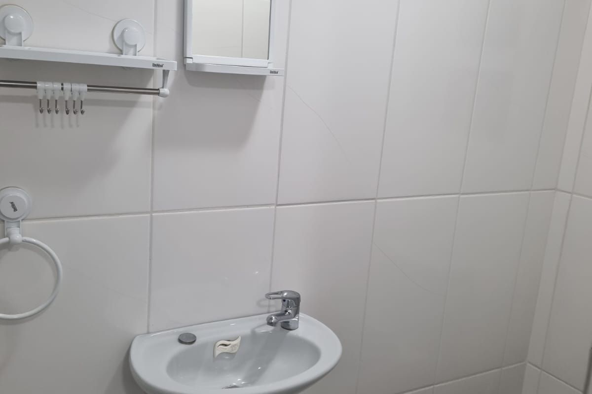 A functional bathroom featuring a wall-mounted basin, chrome faucet, and white ceramic wall tiles with a decorative border.