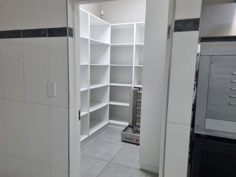 A clean, functional scullery or pantry area featuring white built-in shelving, tiled walls, and durable floor tiles, suitable for organized storage.