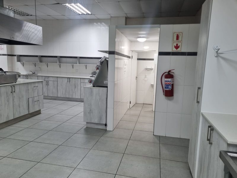 A clean, functional commercial kitchen featuring tiled surfaces, stainless steel extractor hood, and ample built-in cabinetry for efficient food preparation.