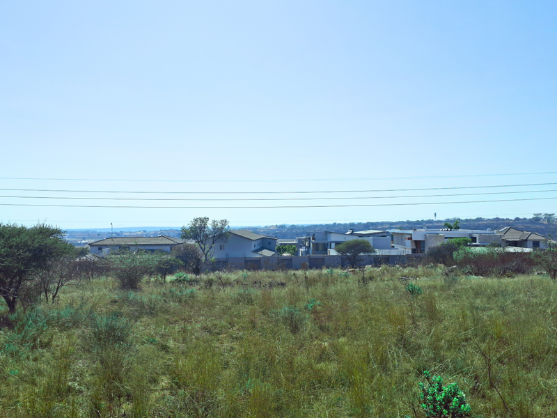 A view of an undeveloped commercial land plot featuring natural vegetation and overhead power lines with surrounding residential development in the distance.