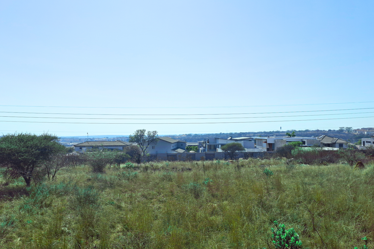 A view of an undeveloped commercial land plot featuring natural vegetation and overhead power lines with surrounding residential development in the distance.