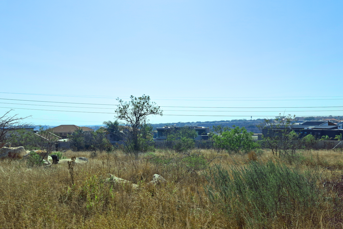 A view of an undeveloped commercial vacant land plot featuring natural vegetation and surrounding residential development in the distance.