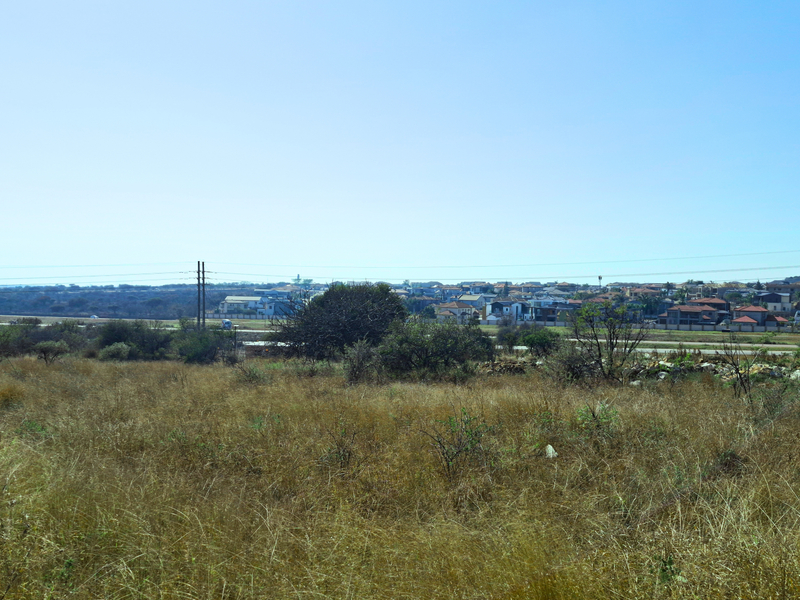 A wide-angle view of an undeveloped commercial land plot with surrounding residential neighborhood and power lines visible in the distance.