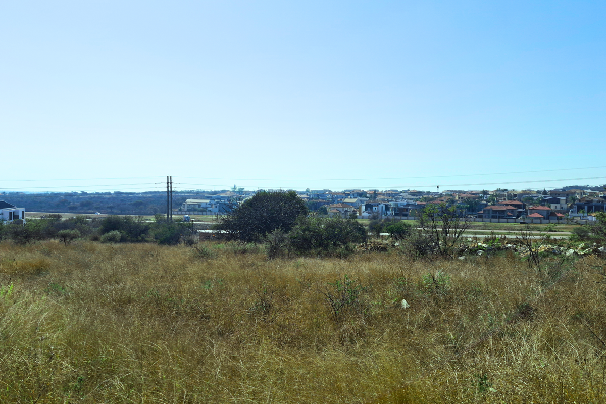 A wide-angle view of an undeveloped commercial land plot with surrounding residential neighborhood and power lines visible in the distance.