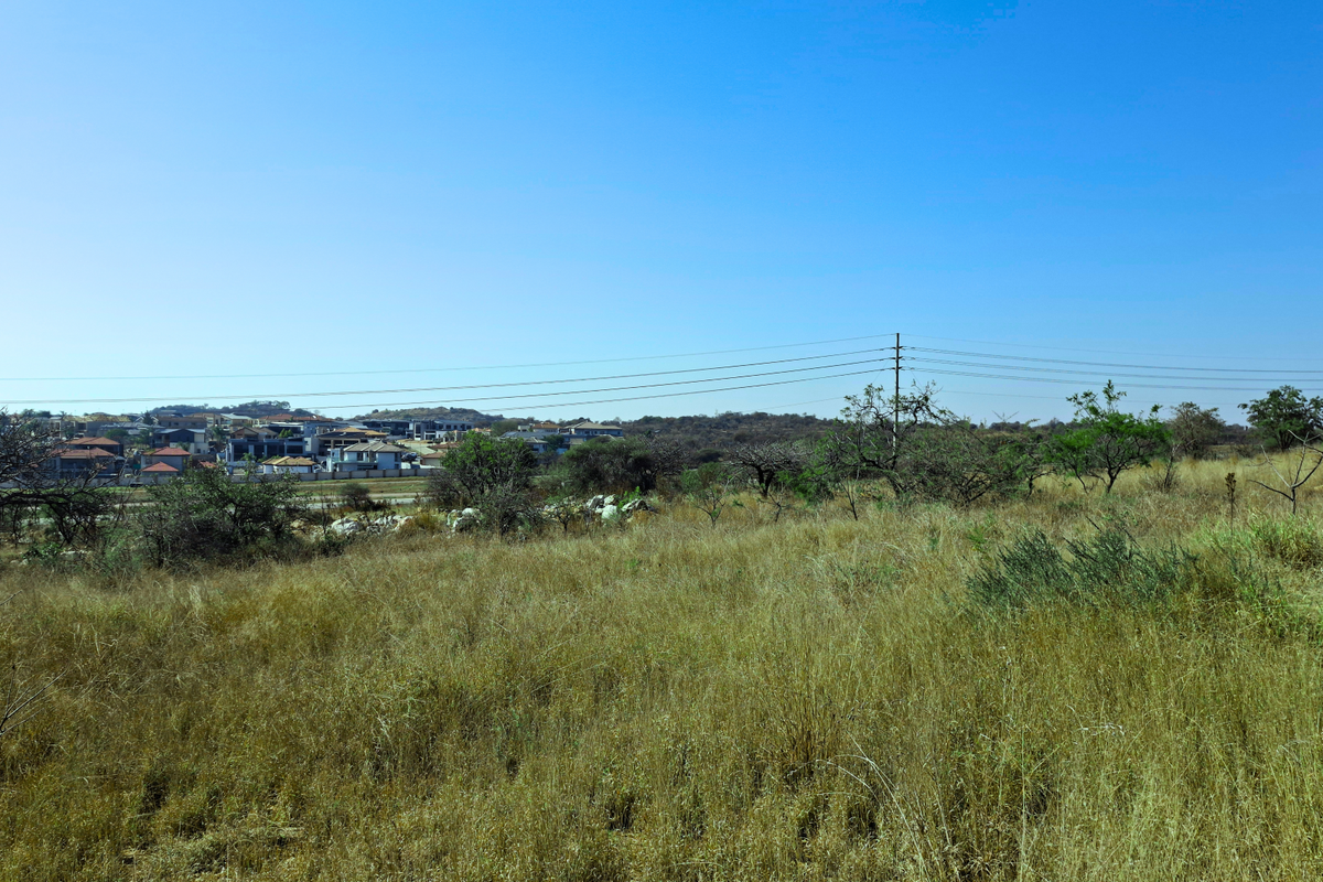 A wide-angle view of the vacant commercial land featuring natural vegetation and overhead power lines with a residential area visible in the distance.