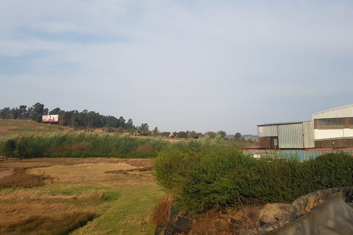 A wide-angle view of the industrial property grounds, featuring open land, natural vegetation, and a metal-clad industrial structure in the background.
