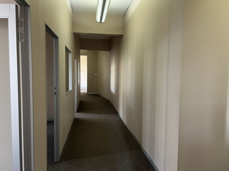 A vacant commercial hallway featuring neutral wall finishes, carpeted flooring, and overhead fluorescent lighting, providing access to multiple office or utility rooms.