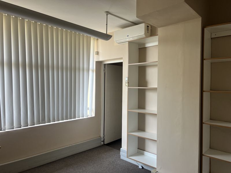 A functional office space featuring built-in shelving, vertical blinds, and a wall-mounted air conditioning unit, ready for professional use.