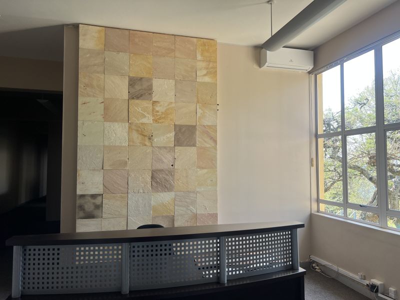 A bright office space featuring a decorative stone feature wall, large windows for natural light, and a built-in reception desk.