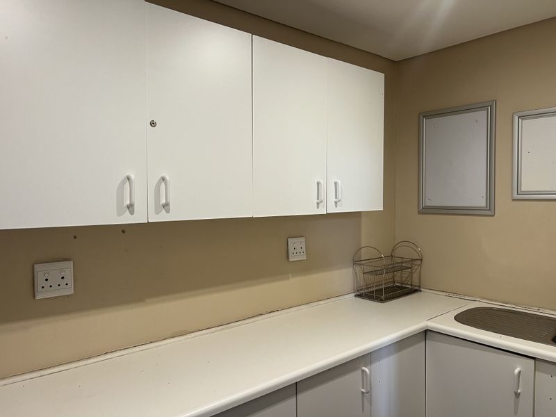 A functional scullery area featuring built-in cabinetry, a laminate countertop, and a stainless steel sink, providing practical utility space.