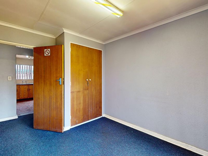 An empty bedroom featuring built-in wooden cupboards, carpeted flooring, and coved cornicing, with a view into an adjacent kitchen area.