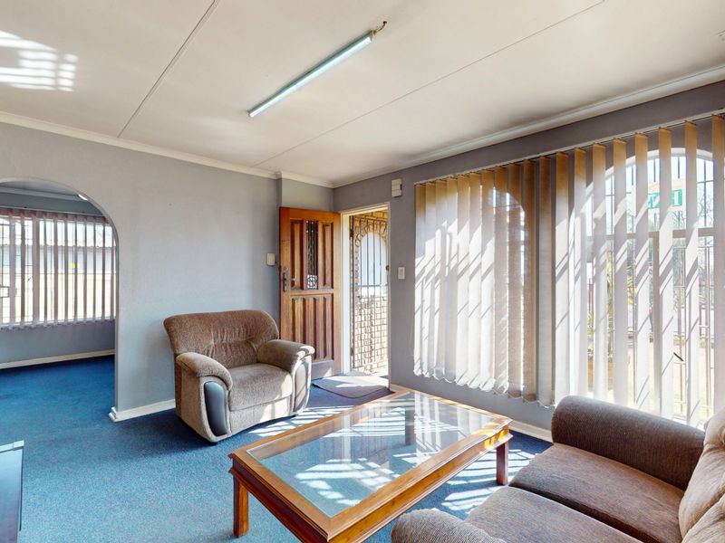 A living room area featuring an arched entryway, security gate, and large windows with vertical blinds, finished with blue carpeting.
