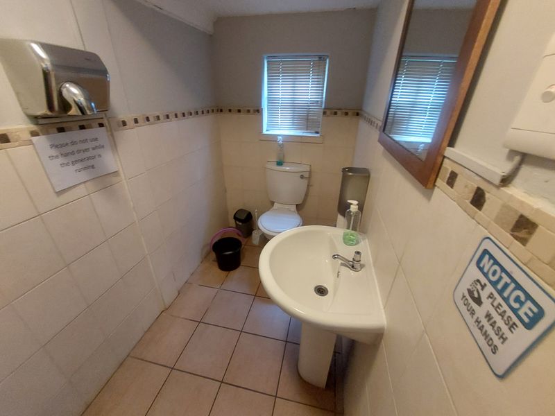 A functional commercial restroom featuring a pedestal sink, toilet, and wall-mounted hand dryer with tiled walls and flooring.