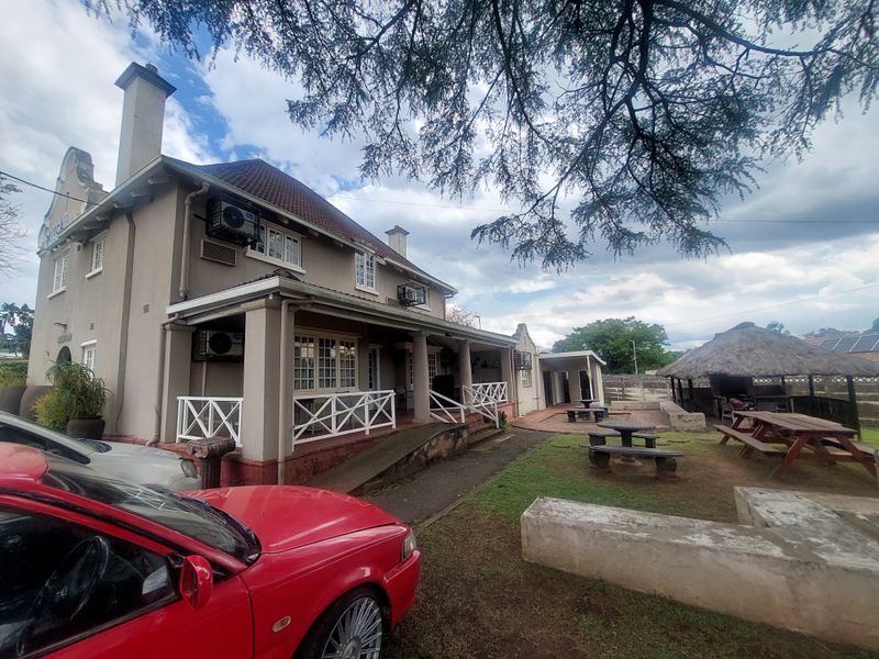 Exterior view of a commercial property featuring a covered veranda, tiled roof, and an adjacent outdoor entertainment area with a thatched lapa.