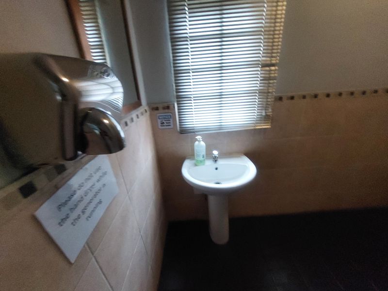 A commercial restroom featuring a pedestal sink, wall-mounted hand dryer, and window blinds.
