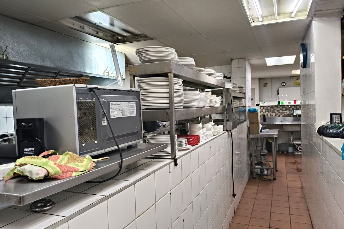 Commercial kitchen area featuring tiled walls, stainless steel prep surfaces, and a dedicated wash-up station with industrial-grade fixtures.