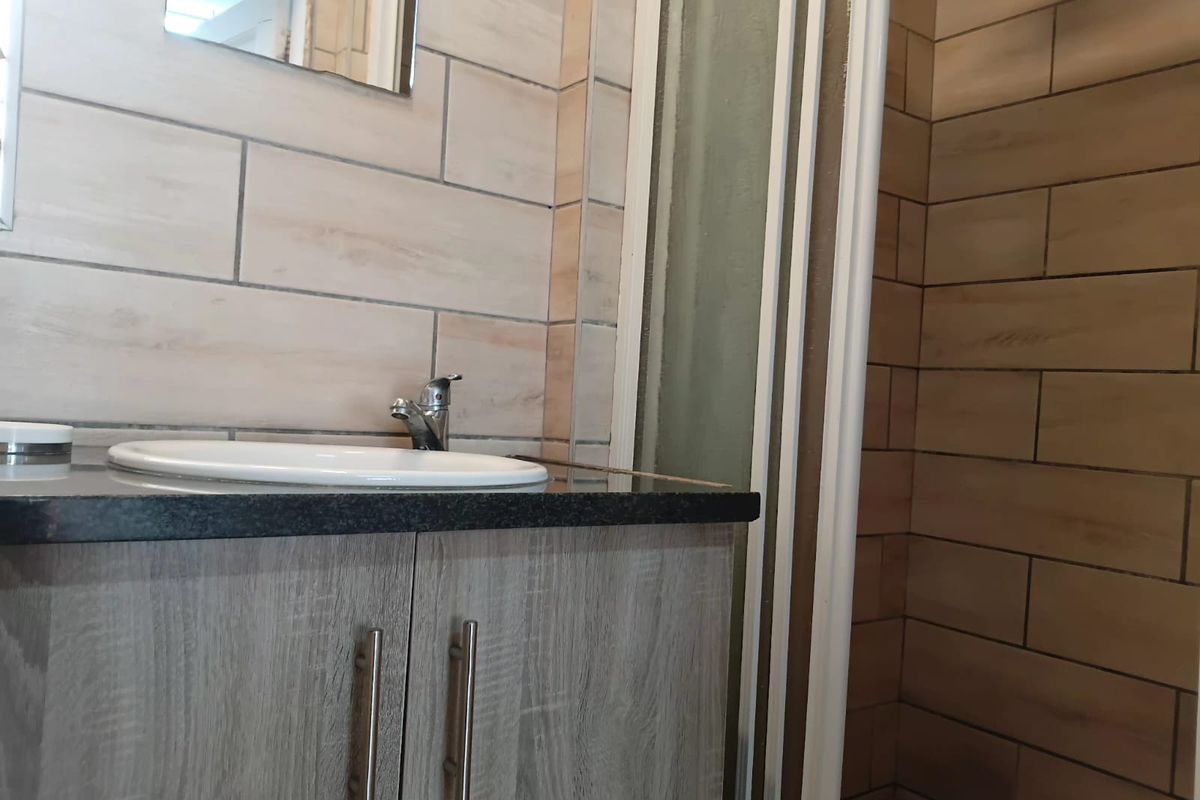 A modern bathroom featuring a vanity cabinet with a granite countertop, drop-in basin, and a separate shower enclosure with tiled wall finishes.