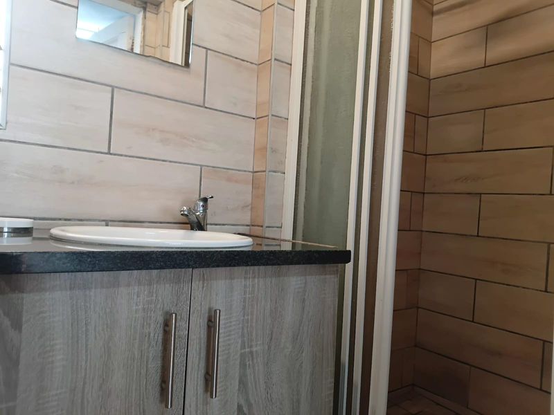 A modern bathroom featuring a vanity cabinet with a granite countertop, drop-in basin, and a separate shower enclosure with tiled wall finishes.