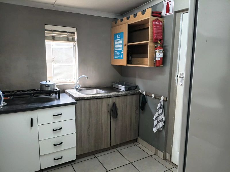A functional office kitchenette featuring a stainless steel sink, laminate countertops, built-in cabinetry, and tiled flooring, equipped with essential fire safety equipment.