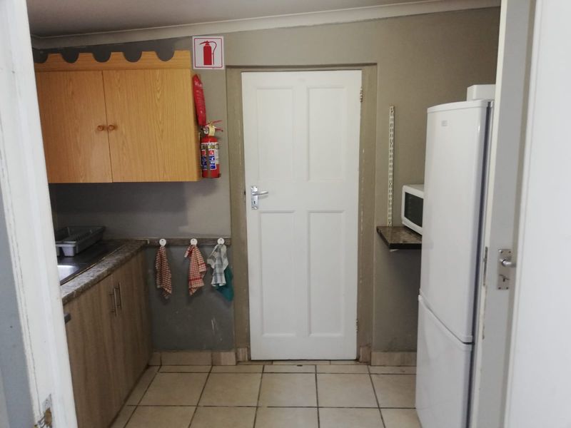 A functional office kitchenette featuring built-in cabinetry, a stainless steel sink, tiled flooring, and essential fire safety equipment.