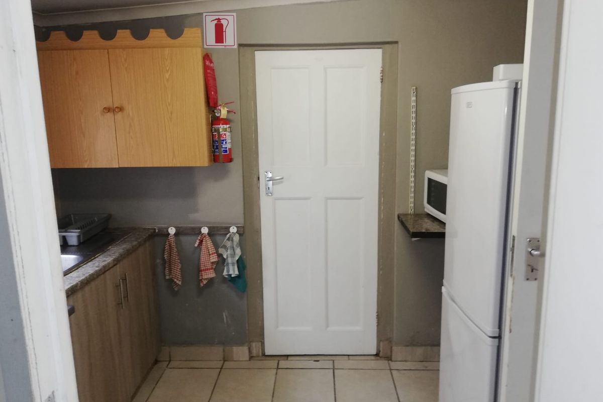 A functional office kitchenette featuring built-in cabinetry, a stainless steel sink, tiled flooring, and essential fire safety equipment.