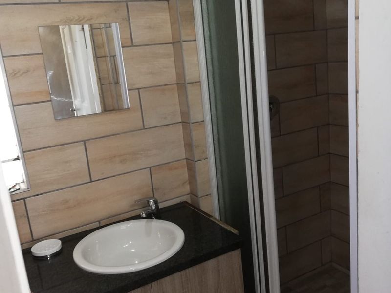 A compact office bathroom featuring a vanity cabinet with a granite countertop, drop-in basin, and a separate shower enclosure with tiled walls.