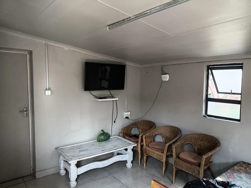 A functional office space featuring tiled flooring, a top-hung window, and surface-mounted electrical conduit, providing a basic workspace environment.