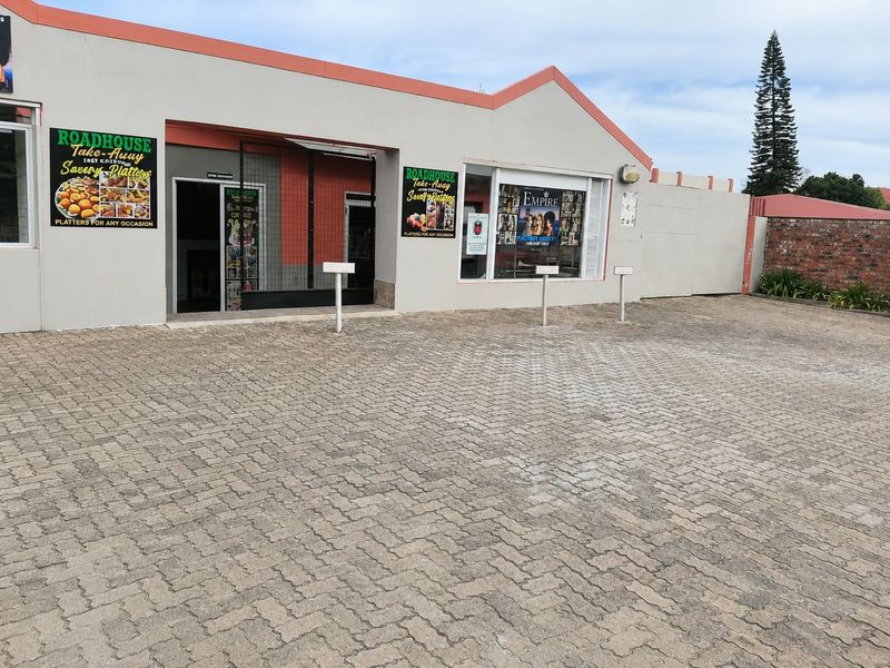 Front exterior view of a commercial office or retail property featuring a paved parking area, security gate, and large display windows.