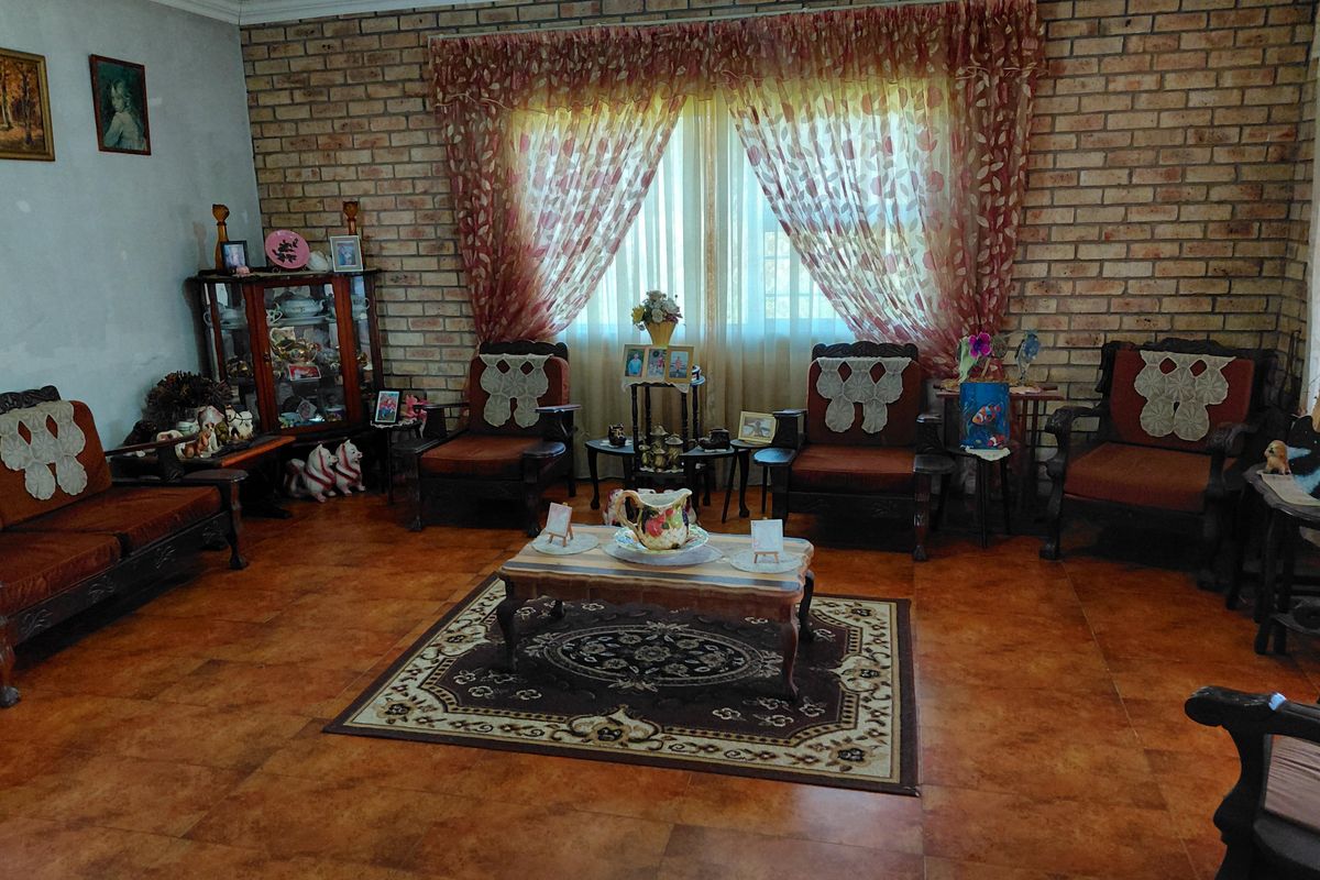 A living room featuring an exposed brick feature wall, large window with curtains, and durable ceramic floor tiles.