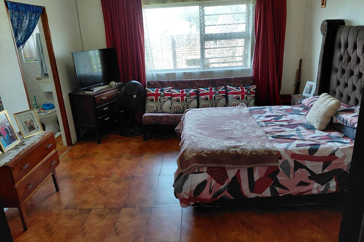 A bedroom featuring tiled flooring, a window with security bars, and direct access to an en-suite bathroom.