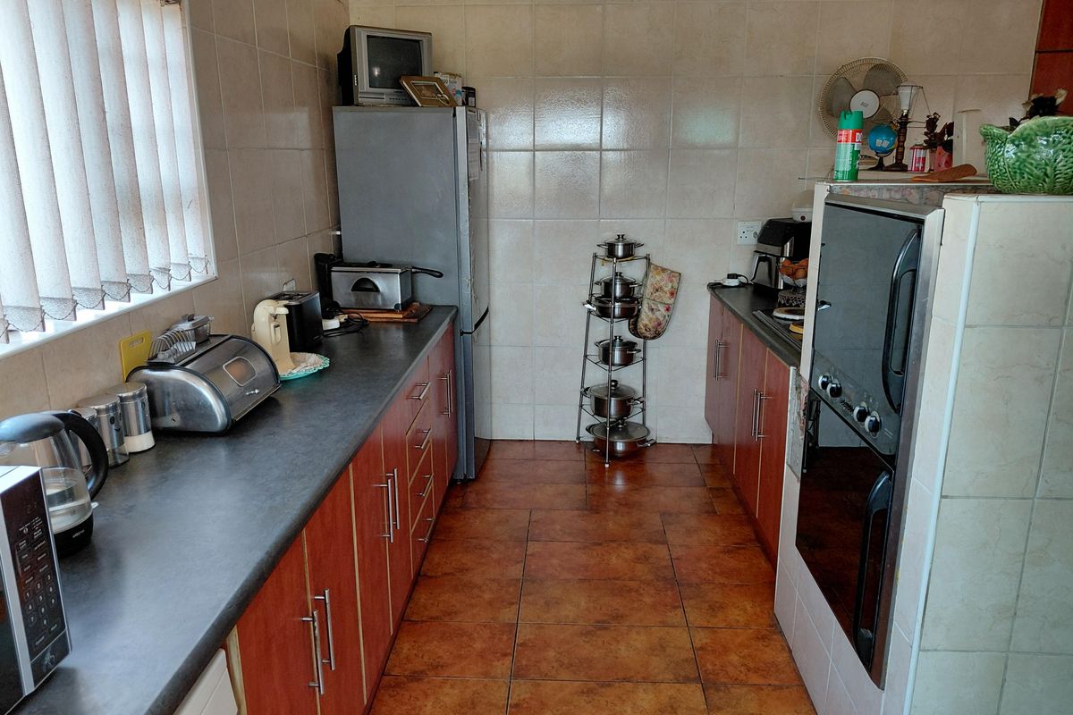 A functional galley-style kitchen featuring wood-finish cabinetry, dark laminate countertops, tiled backsplash, and tiled flooring with a built-in oven.