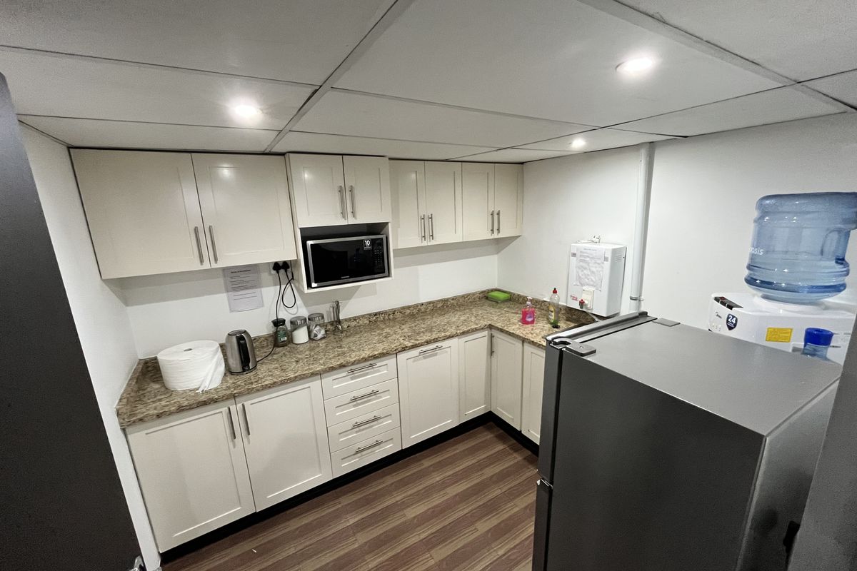 A functional office kitchenette featuring laminate cabinetry, granite-look countertops, a built-in microwave, and a drop ceiling with recessed lighting.