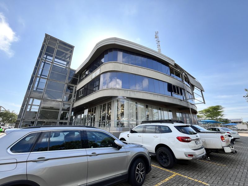 Modern multi-story office building featuring a curved glass facade, prominent glass elevator shaft, and paved parking area.