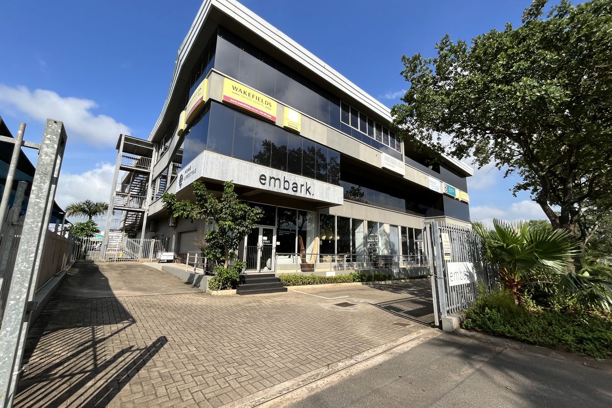 Modern multi-story commercial office building featuring glass curtain walls, paved driveway access, and secure perimeter fencing.