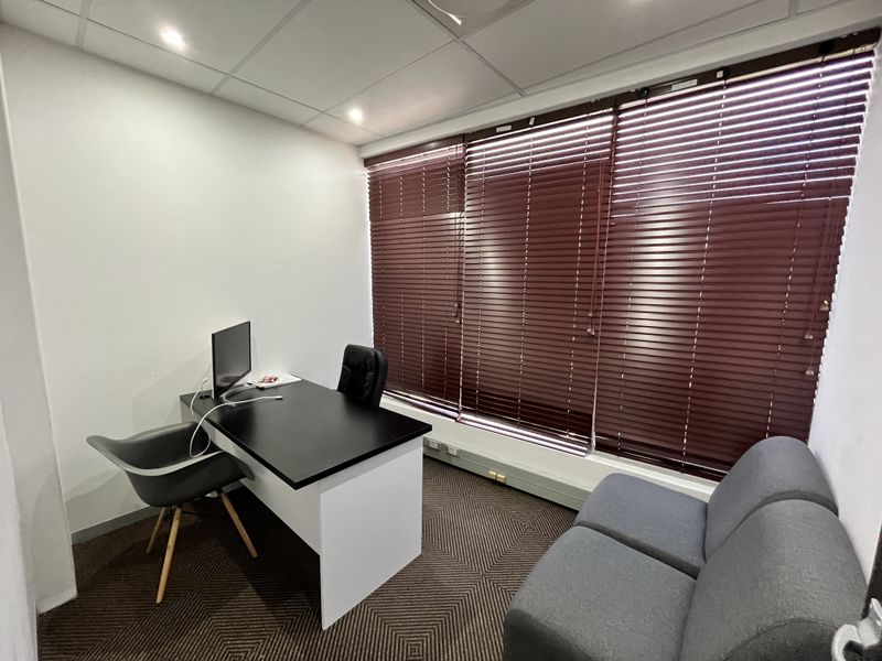 A functional office space featuring a suspended ceiling, recessed lighting, and large windows fitted with horizontal blinds.