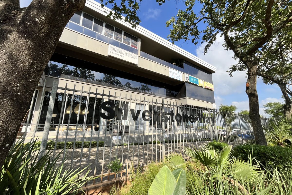 A modern multi-story office building facade featuring glass curtain walls, metal security fencing, and prominent signage, set within a landscaped commercial environment.