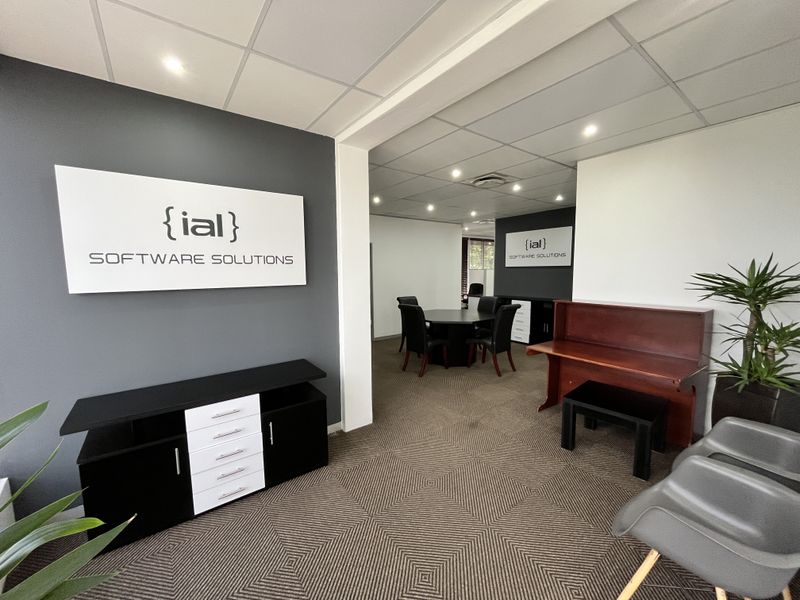 A professional office reception area leading into a connected meeting room, featuring carpeted flooring and recessed ceiling lighting.