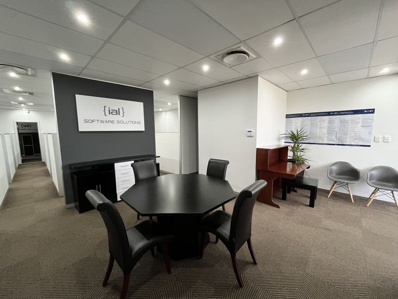 A professional office meeting area featuring a central table, recessed ceiling lighting, and a branded feature wall in a modern corporate workspace.