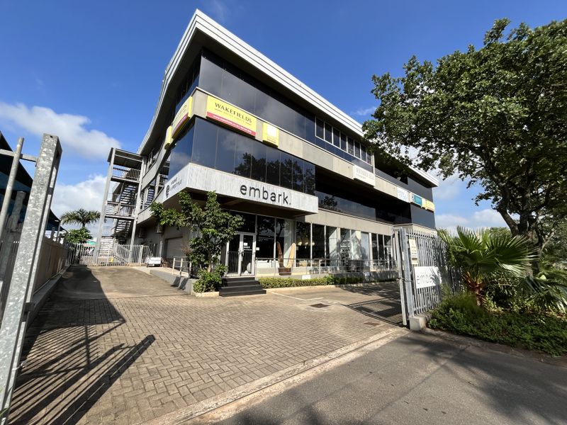 Modern multi-story commercial office building featuring glass curtain walls, paved driveway access, and secure perimeter fencing.