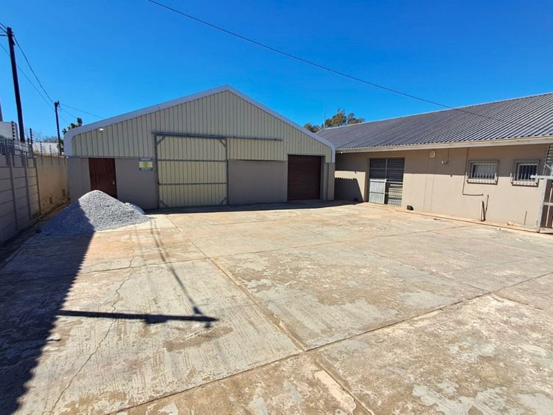 Exterior view of a commercial property featuring a large concrete yard, metal warehouse structure, and perimeter security fencing.