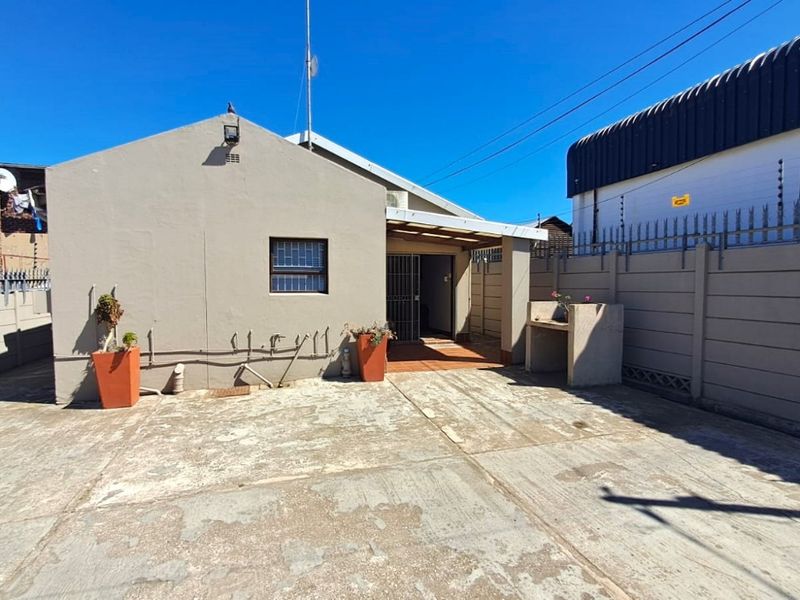 Rear exterior view of the property featuring a paved courtyard, covered patio area, and built-in outdoor braai structure enclosed by perimeter walling.