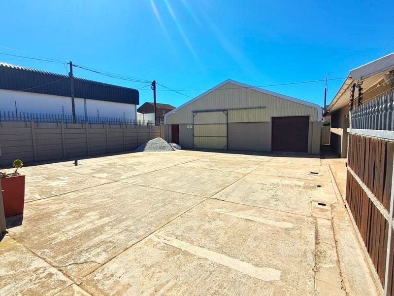 Spacious paved rear yard area featuring a large industrial-style storage building with sliding doors and secure perimeter walling with electric fencing.