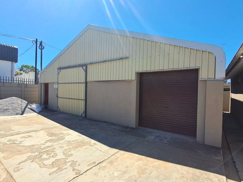 Exterior view of a commercial warehouse or garage facility featuring a roller shutter door, sliding access door, and concrete paved yard area.