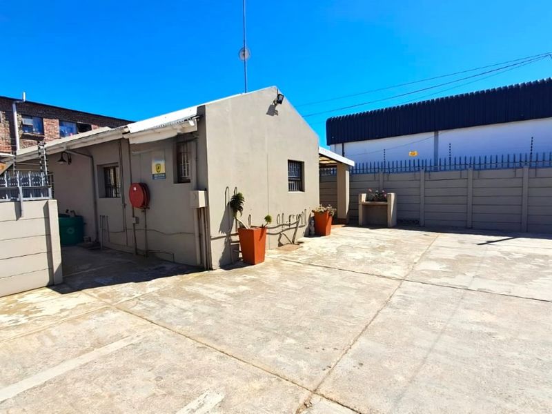 Exterior rear view of the business property featuring a paved courtyard, perimeter wall with security fencing, and a built-in outdoor braai area.