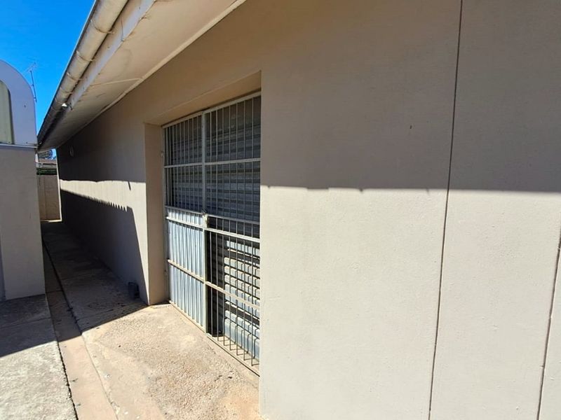 Exterior view of a side passage featuring a secure metal gate and concrete pathway along the building wall.